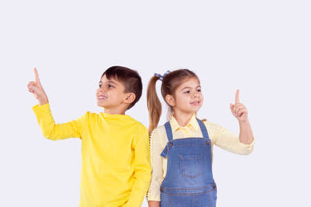 Picture of two schoolchildren boy and girl standing shoulder to shoulder with joy facial expression holding their index fingers up.の写真素材