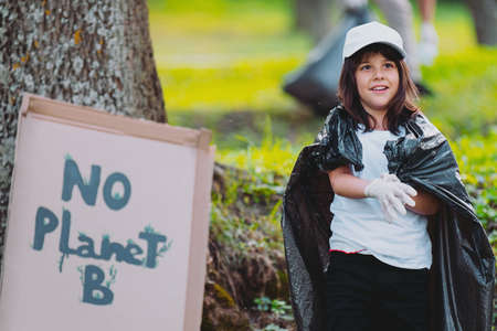 Close up photo of a young girl in a white cap and protective gloves covered her shoulders with a garbage bag and a banner with the inscription attached to the tree, theme to protect the environment.の写真素材
