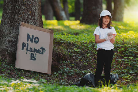 Full-length photo of a happy girl volunteer standing on the ground outdoors, participate in gathering garbage and cardboard banner attached to a tree with the inscription No Planet B.の写真素材