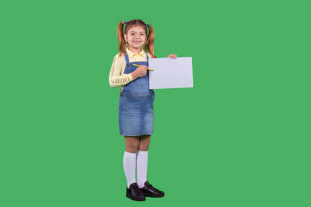Full-length photo of a school girl wearing jeans sundress with two ponytails having joy facial expression and pointing with the pen at the white paper in her hand.の写真素材