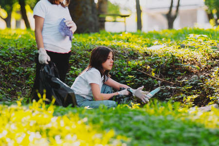 Voluntary project, beautiful female volunteers looking pensively, picking up plastic rubbish and used medical masks into the garbage bag.の写真素材