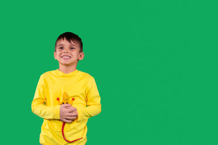 Joyful kid wearing yellow hoodie having smiling facial expression holding the dinosaur toy in his hands, copy space.の写真素材
