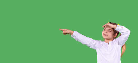 Banner, long format. Schoolgirl wearing white blouse pointing finger aside standing on green studio background, back to school, empty space.の写真素材