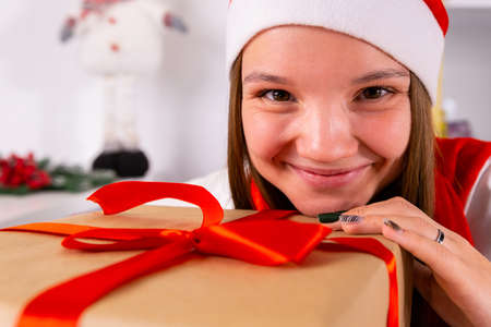 Close up photo of a beautiful girl in a Santa hat touches the present box with her chin and hand with colored manicure.の写真素材