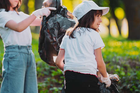 Back view photo of a pretty girl looking to a side with another girl stands with a garbage bag in her hands for gathering rubbish.の写真素材