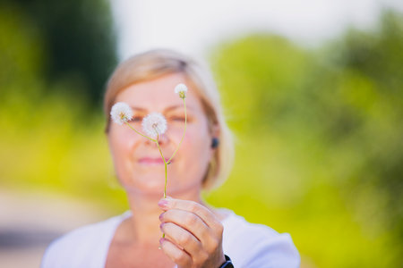 Blurred photo of a blonde woman outdoors holding the dandelion flower in her hand and wearing smart watch and headphones.の写真素材