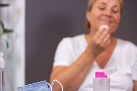 Blurred photo of a woman having acne disease on her face after taking off medical mask and she dabs her face with cosmetic lotion using cotton pad.の写真素材