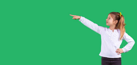 Banner, long format. Side space photo of a schoolgirl wearing school uniform turned her head to the side with one hand pointing using index finger to the side and the other hand keeping on her belt.の写真素材