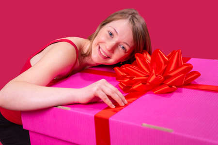 Close up photo of a beautiful happy young woman keeping her head on the big present box of pink color and with bow on that box.の写真素材