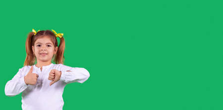 Banner, long format. Side space photo of a school girl in school uniform with two ponytails and yellow ribbon on the head showing hand sign contradiction holding thumbs up and down.の写真素材