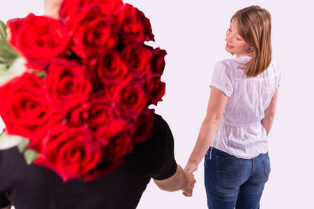 Back view photo of a blonde woman looks over her shoulder and holding the delivery man hand, he is keeping a big bouquet of roses for the woman on his shoulder.の写真素材