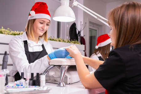 Young woman came in a beauty salon to make manicure for the new year holidays by a professional manicurist woman, gentle care of nails in a beauty salon.の写真素材