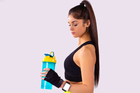 The profile photo of a sporty slim girl long ponytail wearing black top, gloves with smart watch on her hand keeping a bottle of water in one hand and looking at it.の写真素材