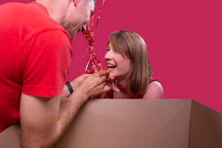 Close up photo of a smiling happy young blonde lady and a man in rad t-shirt putting the ring on her girlfriend finger, she accepted the marriage proposal.の写真素材