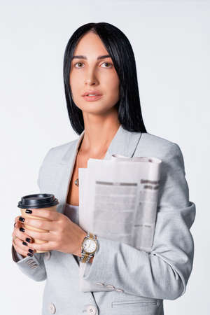 Business partner woman with cup of coffee and newspaper dressed in a modern light suit wearing the gold watch and having black manicure.の写真素材