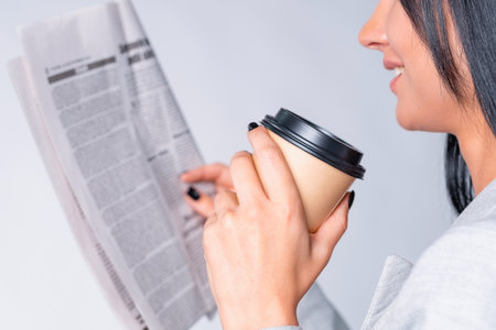 Cropped side view photo of a business lady drinks coffee and reading the newspaper sitting in the office and smiling.の写真素材
