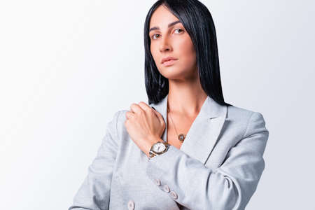 close up photo of a beautiful business woman with black long hair posing for camera in a modern light jacket wearing gold watch and pendant on her neck.の写真素材