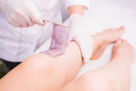 Cosmetologist in beauty clinic performs a depilation procedure for removing waxing hair from the legs using wax violet sugaring paste, beauty and body care concept.の写真素材