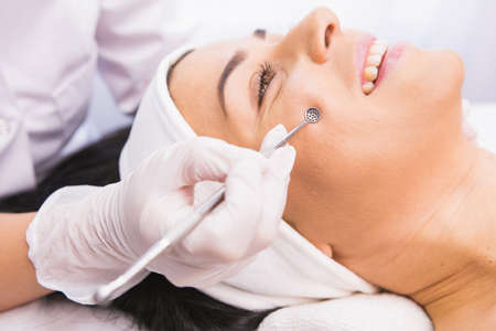 Cosmetician in protective gloves performs a cosmetic procedure on the patients face using medical instrument tool for removal acne, comedones, impurities from the face.の写真素材