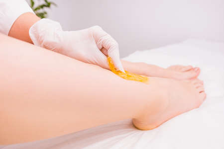 Professional cosmetologist in beauty salon making waxing, an depilation procedure for removing hair from the leg using sugaring paste on white backgroundの写真素材