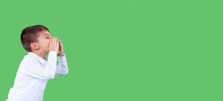 Banner, long format. Side view photo of a school boy in white t-shirt keeping his hands to his mouth and is shouting, side space for the text.の写真素材