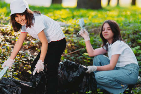 Close up photo of two pretty girls participate in gathering the rubbish and used medical masks in garbage black bags having good mood, volunteer mission to keep clean our planet earth from pollution.の写真素材