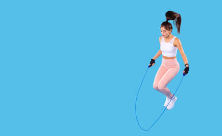 Young sporty girl doing jumping rope exercise at gym on a workout session wearing comfortable sports clothes and white sneakers, on the hand she has digital watch.の写真素材
