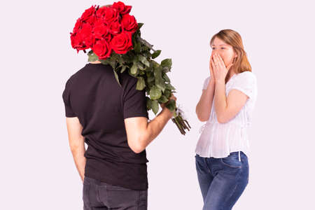 Courier man in black uniform delivered wonderful bouquet of red roses to a amazed blonde woman, she can not believe it and covers her face with her palms.の写真素材