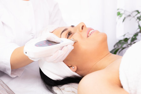 Happy woman, female client getting procedure facial ultrasound cavitation by a cosmetologist in a...