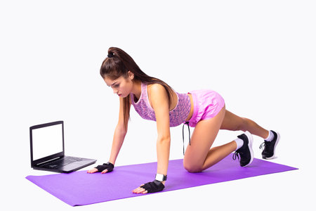 Sportive girl with perfect body making fitness online isolated on the mat standing on the hands and one knee bent forward looking down.の写真素材