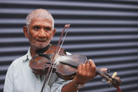 Close up photo of a gray-haired unshaven old man musician holding a wooden violin and playing beautiful melody being outdoors.の写真素材