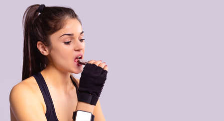 Sporty young brunette girl wearing digital watch on her hand and sports gloves leading a health lifestyle eating dietic cookie.の写真素材