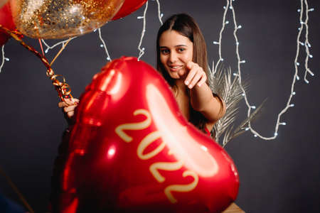 Beautiful young happy girl posing with a heart shaped balloons red color and illumination on the grey background, new year concept.の写真素材