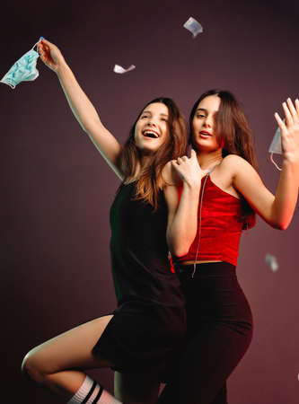 Side view photo of two friends beautiful girls in evening wear happy smiling throwing medical masks in air, ready to party.の写真素材