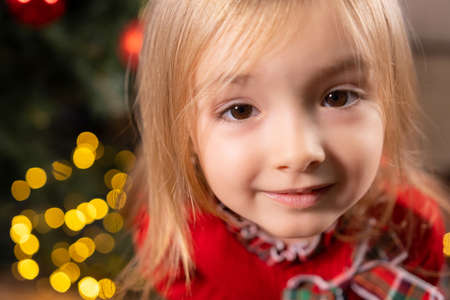 Close up photo of a blonde little girl with beautiful brown eyes joyful looking at the camera over the lights on the background.の写真素材
