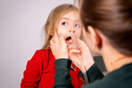 Mother rinse her little girl nose with inhalation apparatus to clean the nose, the girl is calm and doing the procedure.の写真素材