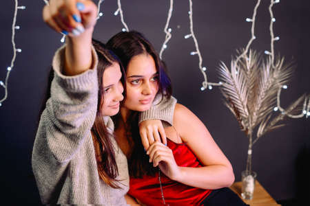 Close up photo of two sisters looking aside one girl raised hand up with blue manicure over grey background and illumination.の写真素材