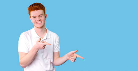 Young handsome man wearing casual white t-shirt smiling happy pointing with his thumbs and indicate fingers at copy space over blue background.の写真素材