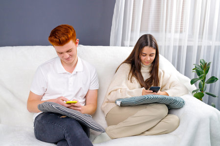 Young couple relaxing and spending time together on the couch while staying at home using smart phones.の写真素材