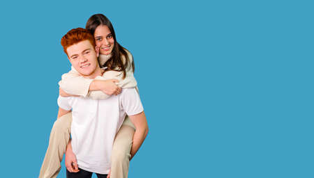 Happy emotions and feelings having a loving couple girl climbed up on the back of her boyfriend over blue background, copy space.の写真素材