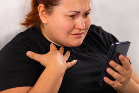Worried big size red hair woman in black t-shirt viewing bad news on the smart phone she holding in her hand.の写真素材