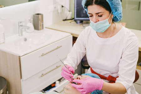 Dentist in a medical mask and pink protective gloves working using dental instruments with man teeth in dental clinic.の写真素材