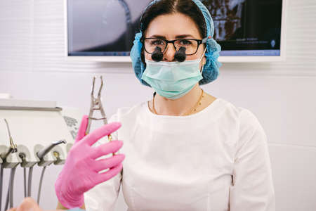 Professional brunette woman dentist smiling to the camera holding dental instruments wearing medical uniform.の写真素材