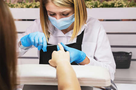 Cosmetologist professional manicurist woman in medical mask and protective gloved making manicure for a client on pandemic time.の写真素材