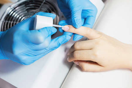 Nail beautician in protective gloves polishing clients nails using brush in beauty salon, beauty nail concept.の写真素材