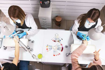Photo from above of two professional manicurist making holiday manicure for two client women in beauty salon on pandemic time.の写真素材