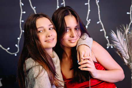 Two girls brunette friends making fun embracing smiling holding hands over grey background and illumination.の写真素材