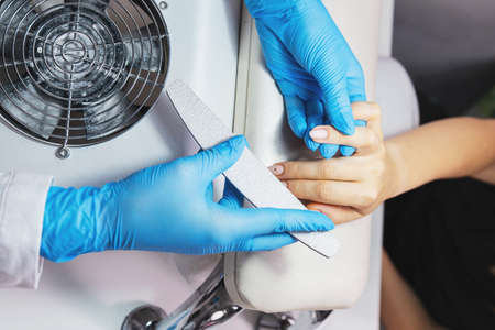 Manicurist filing young woman nails in salon wearing blue protective gloves make nails ready to polish.の写真素材