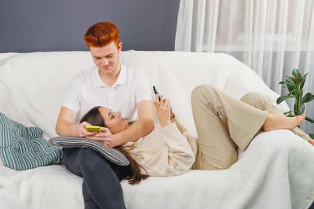 Two loving people relaxing weekend at home on the sofa holding in the hands smart phones and chatting.の写真素材