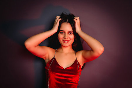 Close up photo of a beautiful happy brunette girl in red clothes touching her hair looking at the camera.の写真素材